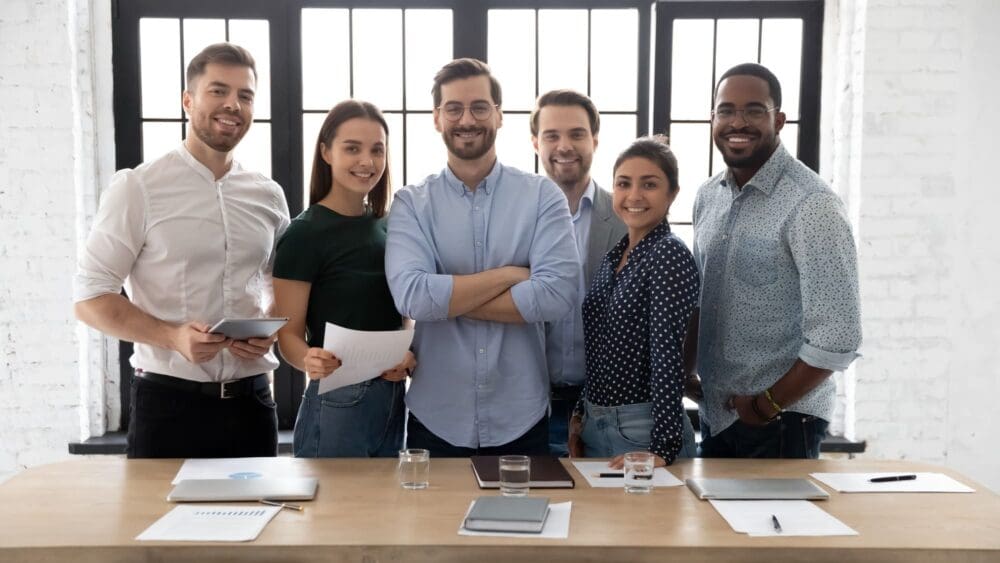 Corporate photo smiling diverse employees with confident executive wearing glasses standing in modern office room